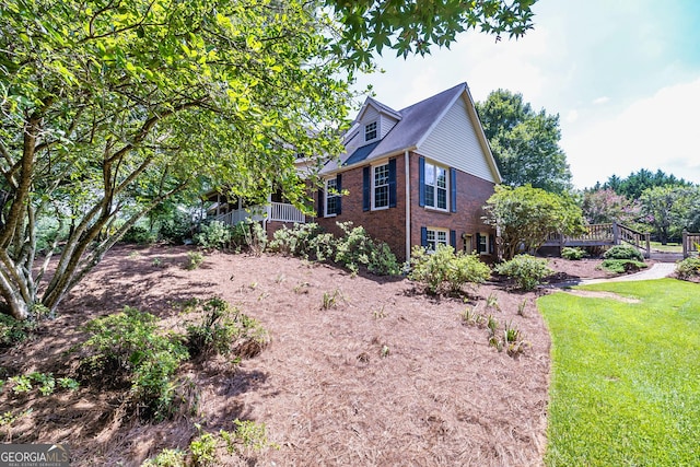 view of property exterior featuring brick siding, a lawn, and a wooden deck