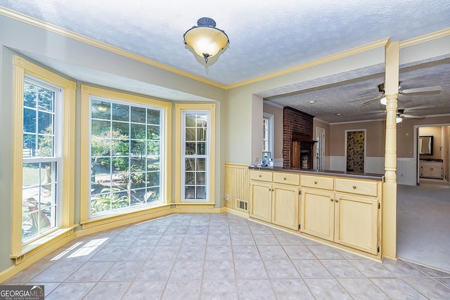 unfurnished dining area with crown molding, light tile patterned floors, a ceiling fan, wainscoting, and a textured ceiling