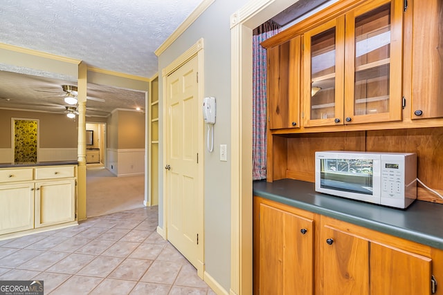 kitchen featuring ceiling fan, light tile patterned flooring, a textured ceiling, and crown molding