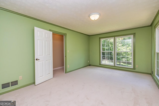 spare room featuring baseboards, visible vents, light colored carpet, crown molding, and a textured ceiling