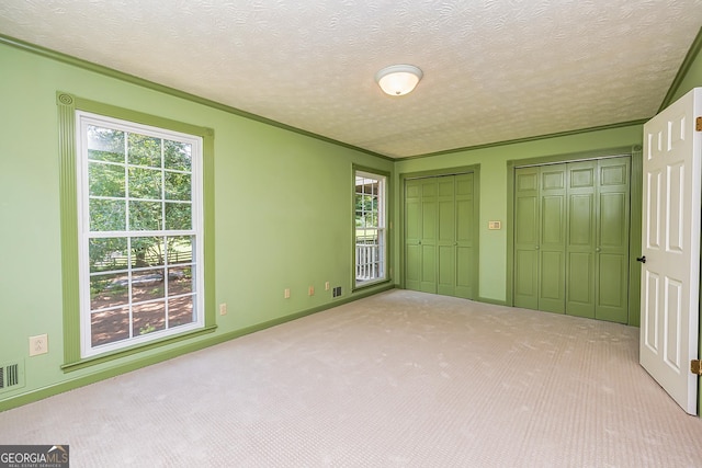 unfurnished bedroom featuring a textured ceiling, multiple windows, multiple closets, and light colored carpet