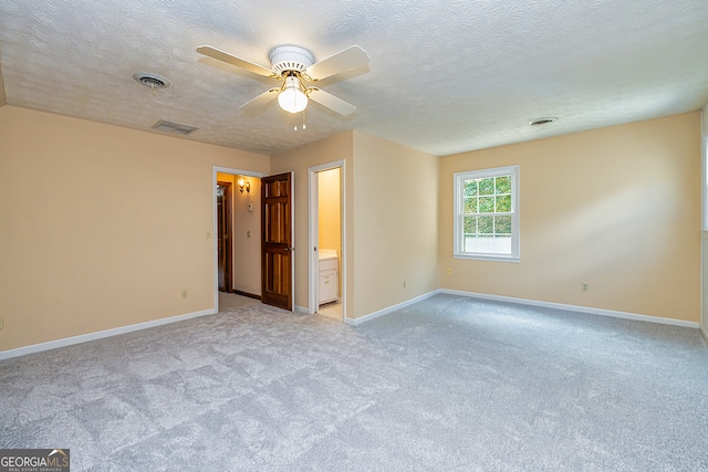 unfurnished bedroom featuring ceiling fan, ensuite bath, a textured ceiling, and light colored carpet