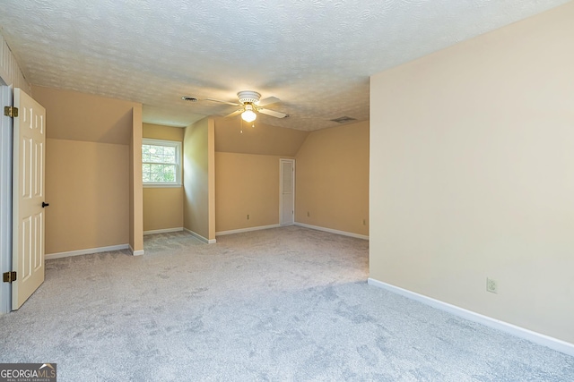 additional living space with a textured ceiling, lofted ceiling, light carpet, visible vents, and baseboards