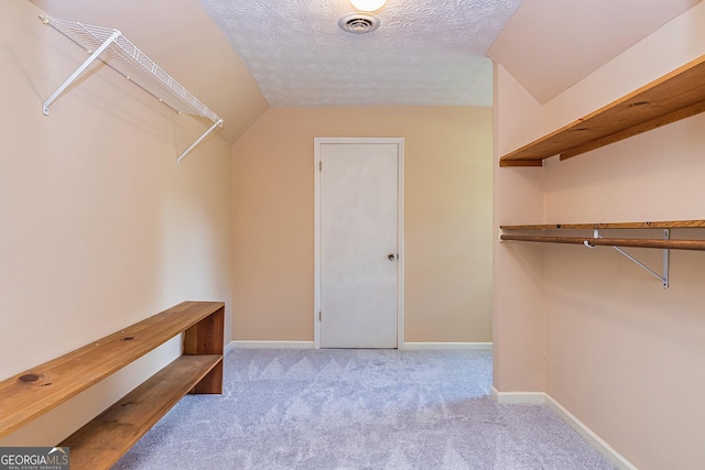 spacious closet featuring light colored carpet, vaulted ceiling, and visible vents