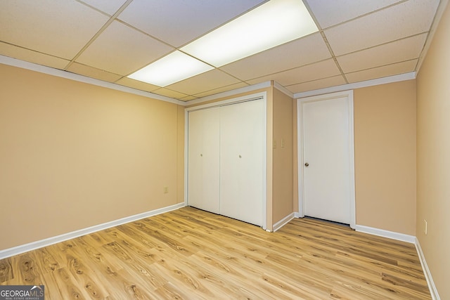 unfurnished bedroom with a drop ceiling, a closet, light wood-type flooring, and baseboards