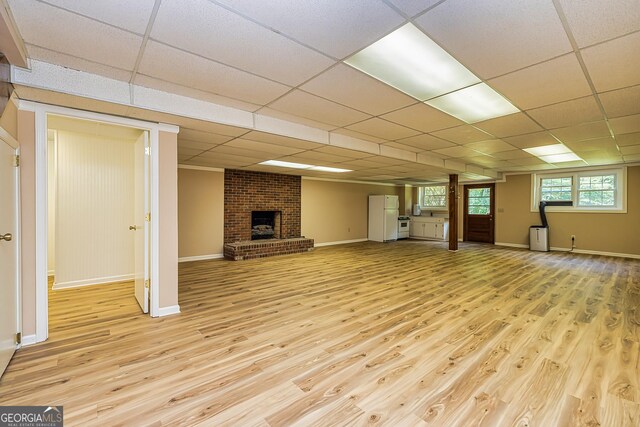 unfurnished living room featuring light wood-style floors, a paneled ceiling, a fireplace, and baseboards