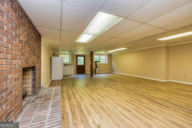 basement featuring a fireplace, a drop ceiling, brick wall, and light hardwood / wood-style floors