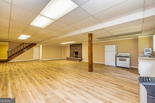 finished below grade area with light wood-style flooring, freestanding refrigerator, a brick fireplace, a sink, and stairs