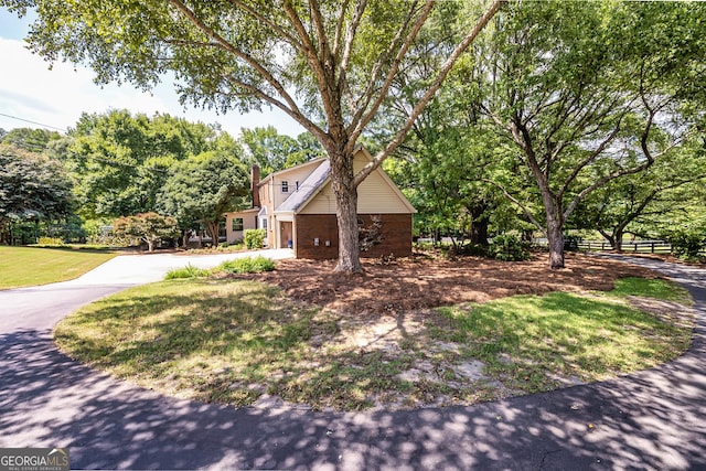 view of front of house with driveway, brick siding, a front lawn, and fence