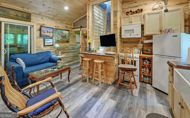 kitchen featuring white appliances, a kitchen breakfast bar, wood-type flooring, vaulted ceiling, and a barn door