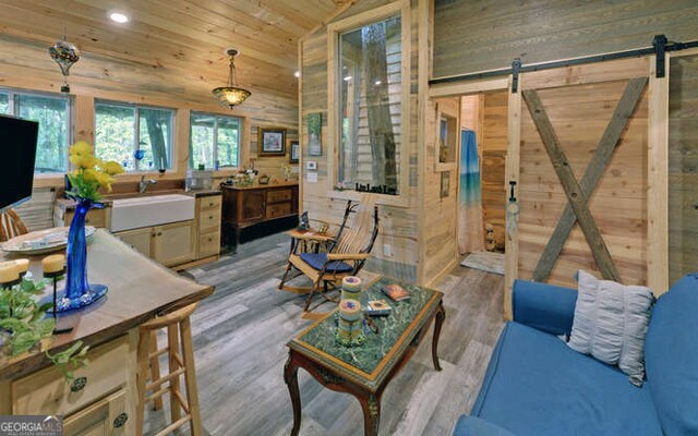 living room with vaulted ceiling, light hardwood / wood-style flooring, wooden walls, and a barn door