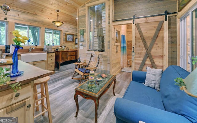 living room featuring wooden walls, sink, a barn door, light hardwood / wood-style flooring, and wood ceiling