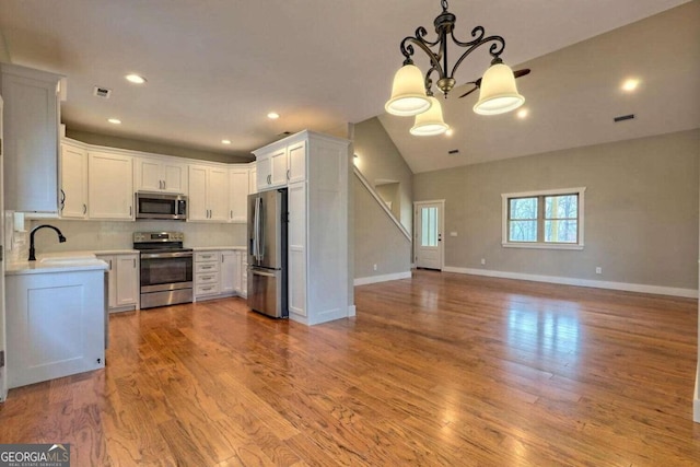 kitchen with white cabinetry, light hardwood / wood-style flooring, hanging light fixtures, and appliances with stainless steel finishes