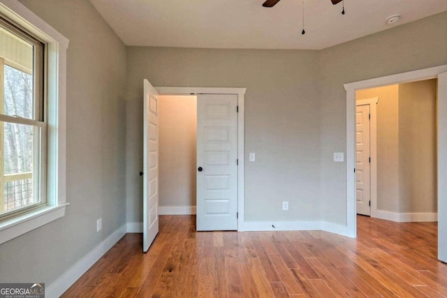 unfurnished bedroom featuring ceiling fan, multiple windows, and hardwood / wood-style flooring