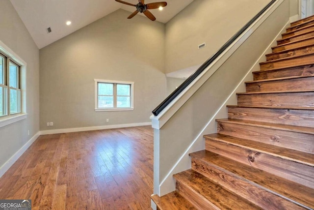 staircase featuring hardwood / wood-style flooring, high vaulted ceiling, and ceiling fan