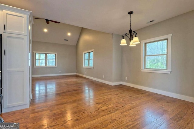 unfurnished room featuring light hardwood / wood-style floors, lofted ceiling, and an inviting chandelier