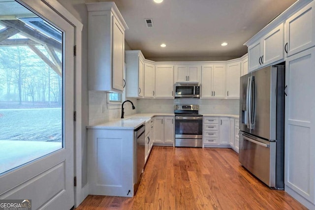 kitchen with white cabinets, appliances with stainless steel finishes, light hardwood / wood-style flooring, and tasteful backsplash