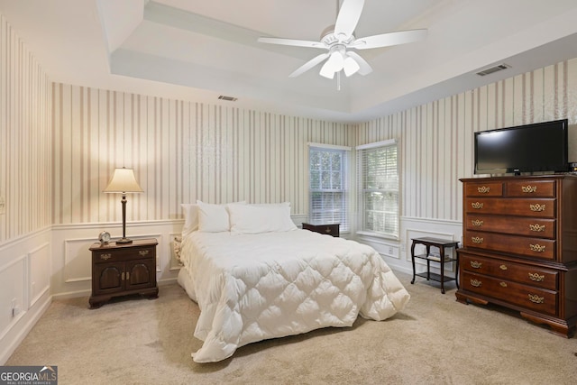 bedroom with light colored carpet, a tray ceiling, and ceiling fan