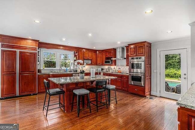 kitchen featuring light stone countertops, wall chimney exhaust hood, dark hardwood / wood-style floors, a kitchen island, and appliances with stainless steel finishes