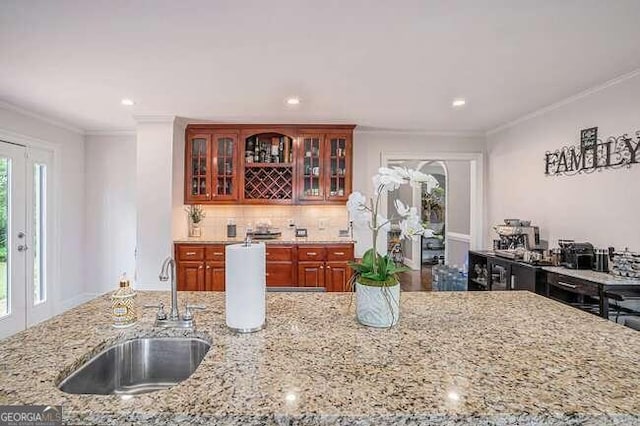 kitchen with backsplash, light stone counters, ornamental molding, and sink