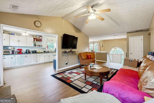 living area featuring visible vents, lofted ceiling with beams, light wood-style floors, a textured ceiling, and baseboards