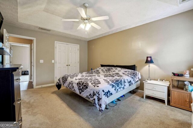 bedroom featuring a textured ceiling, carpet flooring, visible vents, a closet, and a tray ceiling