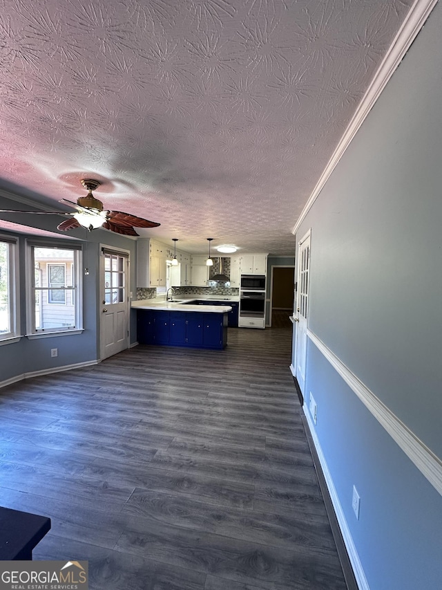 kitchen featuring ornamental molding, open floor plan, dark wood-type flooring, a peninsula, and light countertops