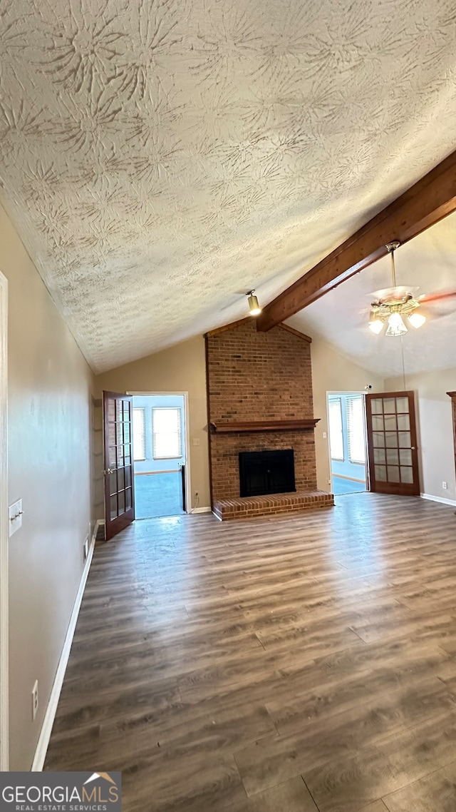 unfurnished living room featuring a textured ceiling, a healthy amount of sunlight, a brick fireplace, and lofted ceiling with beams