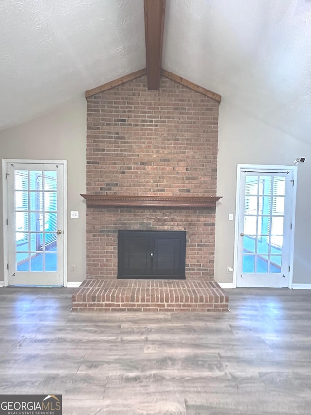 unfurnished living room featuring a healthy amount of sunlight, a fireplace, lofted ceiling with beams, and wood finished floors