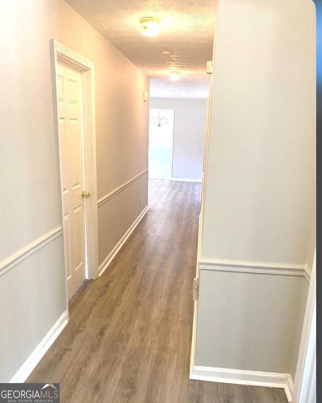 hall with a textured ceiling, wood finished floors, and baseboards