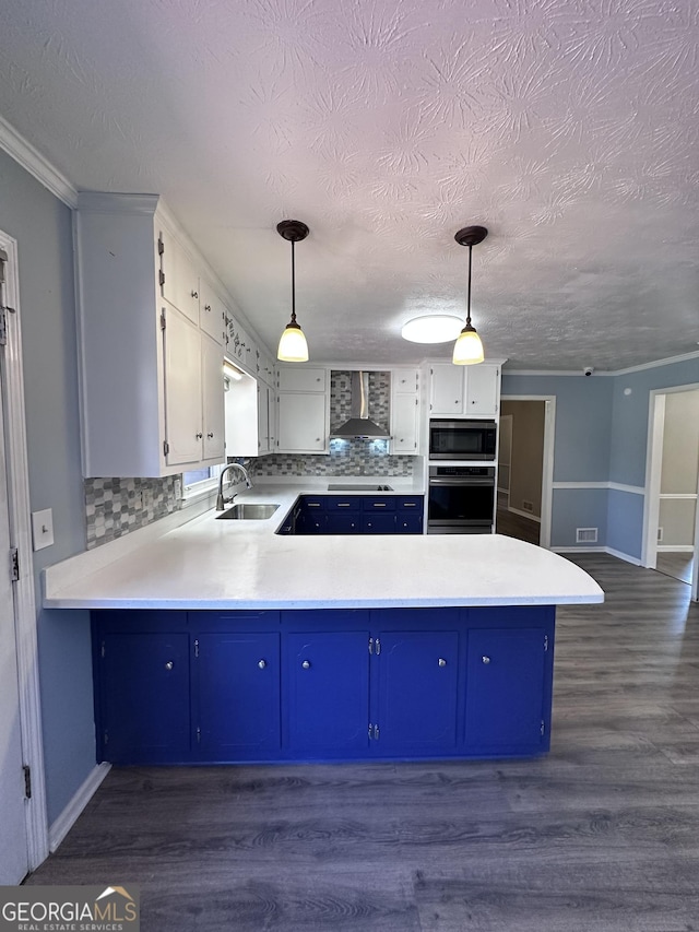 kitchen featuring blue cabinets, a peninsula, a sink, wall chimney exhaust hood, and stainless steel microwave