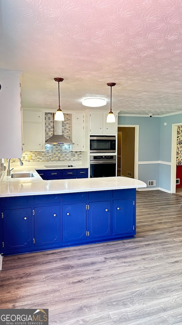 kitchen featuring decorative light fixtures, stainless steel appliances, sink, white cabinetry, and wall chimney range hood