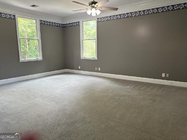 carpeted spare room featuring ceiling fan, ornamental molding, and a wealth of natural light