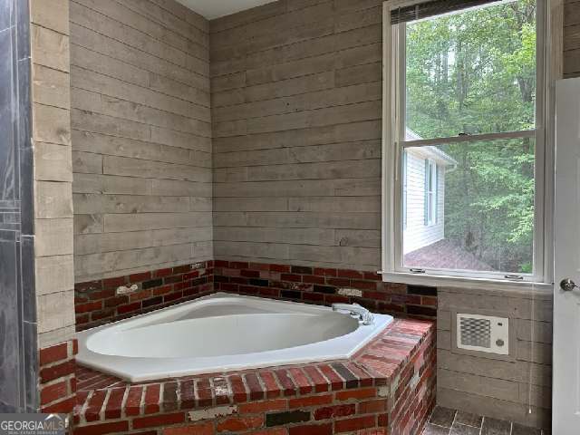 bathroom featuring a relaxing tiled tub and wooden walls