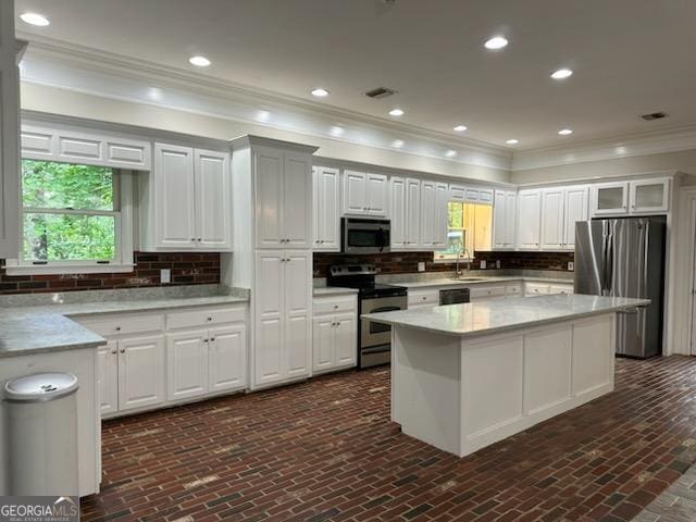 kitchen featuring sink, a center island, stainless steel appliances, light stone countertops, and white cabinets