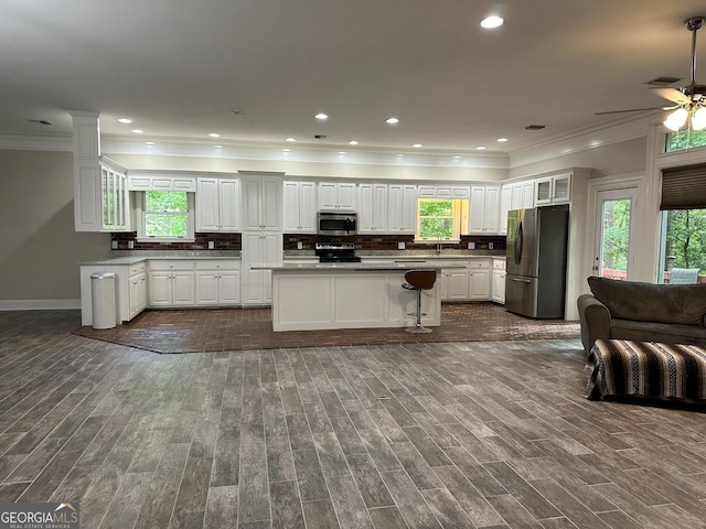 kitchen with appliances with stainless steel finishes, dark hardwood / wood-style floors, tasteful backsplash, a healthy amount of sunlight, and white cabinets