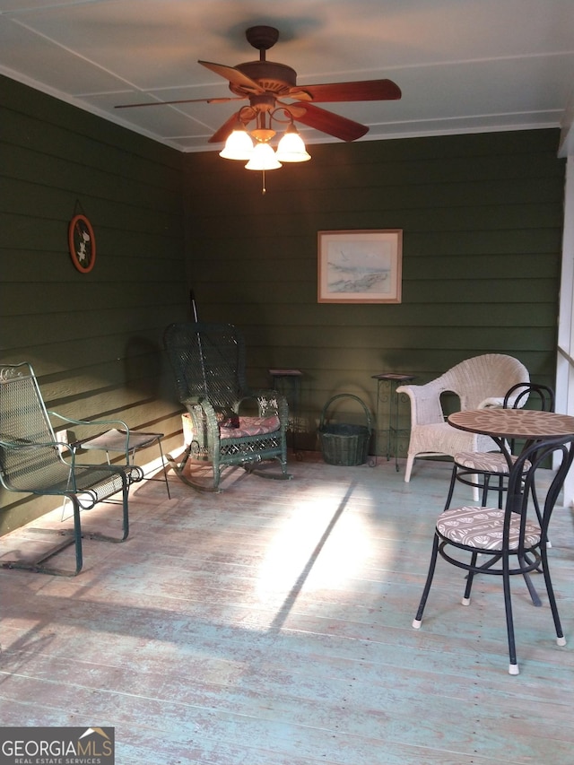 sitting room featuring a ceiling fan, wood walls, and wood finished floors