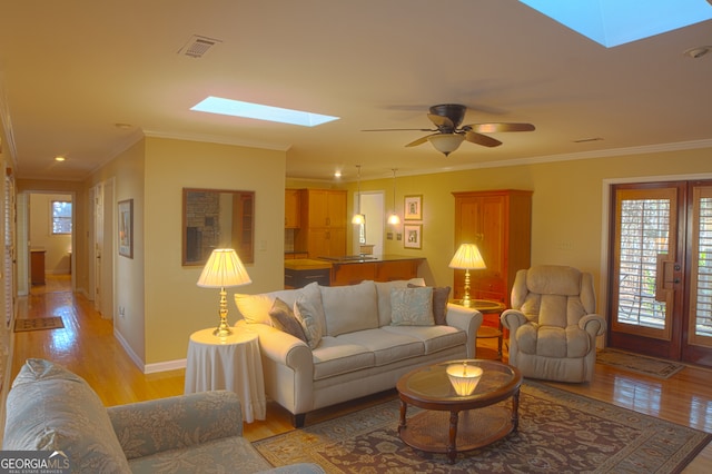 living room with a skylight, light wood-style flooring, visible vents, and crown molding