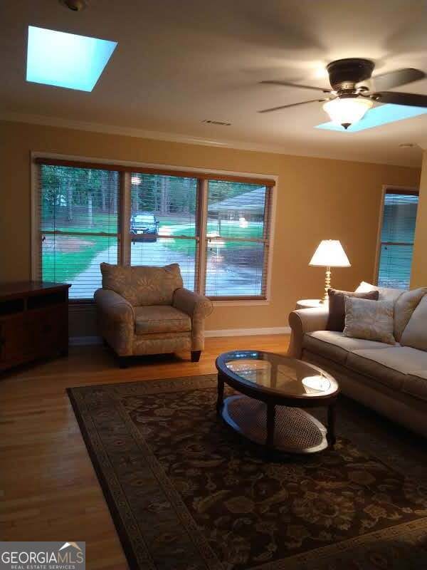 living room featuring a skylight, ceiling fan, wood-type flooring, and ornamental molding