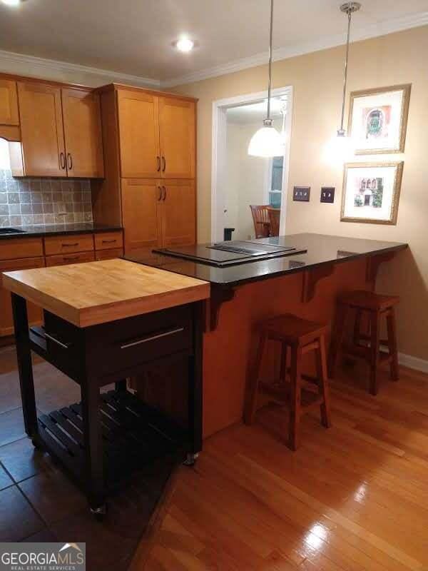 kitchen featuring crown molding, a breakfast bar area, decorative backsplash, wood finished floors, and butcher block countertops