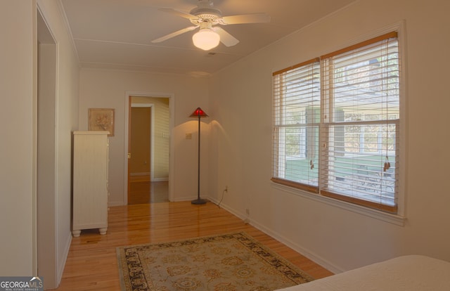 interior space with light wood-type flooring, a ceiling fan, baseboards, and crown molding