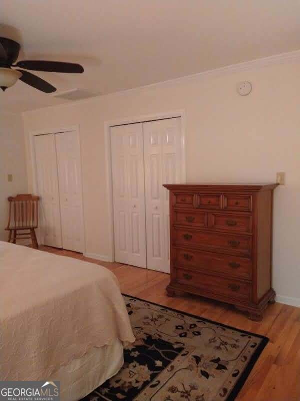 bedroom with multiple closets, ornamental molding, light hardwood / wood-style flooring, and ceiling fan