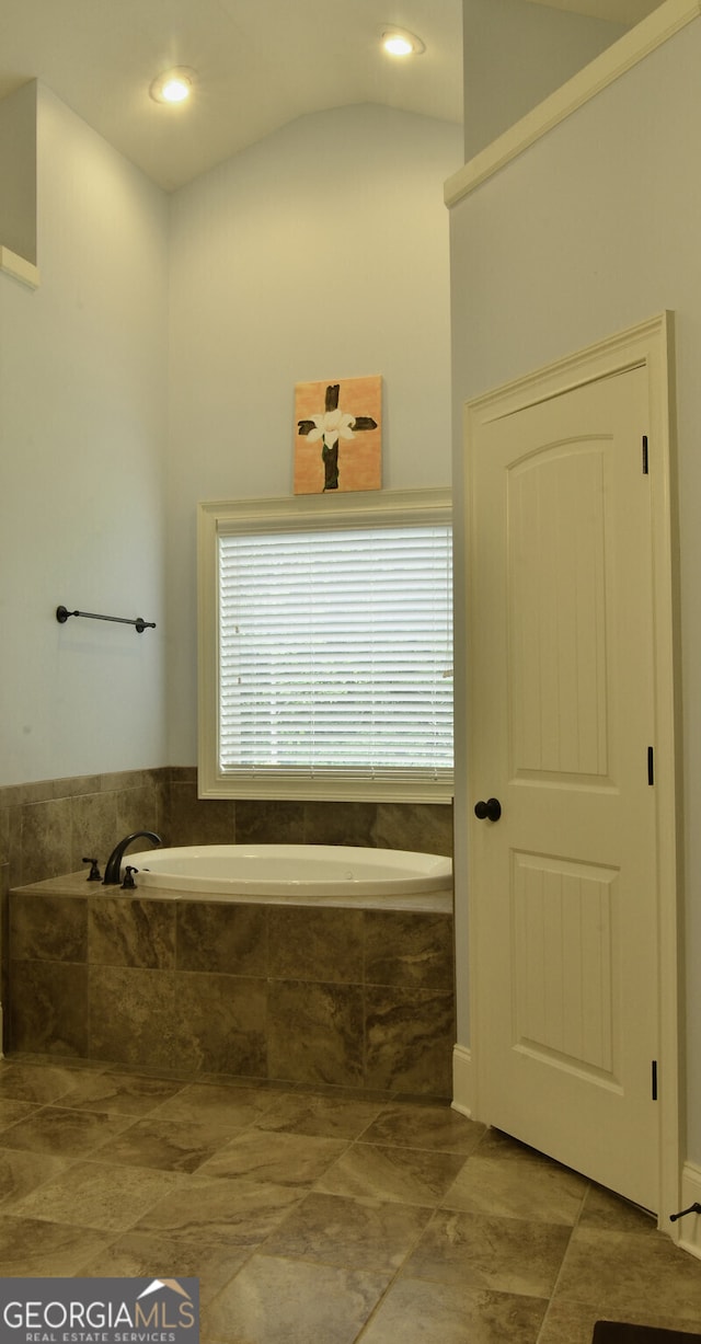 bathroom featuring a relaxing tiled tub, tile patterned flooring, and lofted ceiling