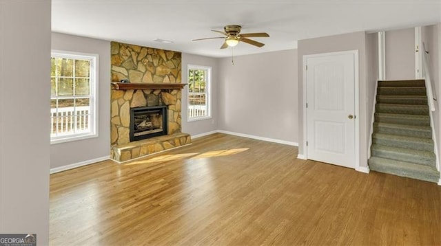 unfurnished living room featuring wood-type flooring, a stone fireplace, and ceiling fan