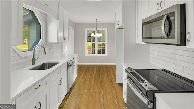 kitchen featuring white cabinetry, sink, light hardwood / wood-style flooring, decorative light fixtures, and appliances with stainless steel finishes