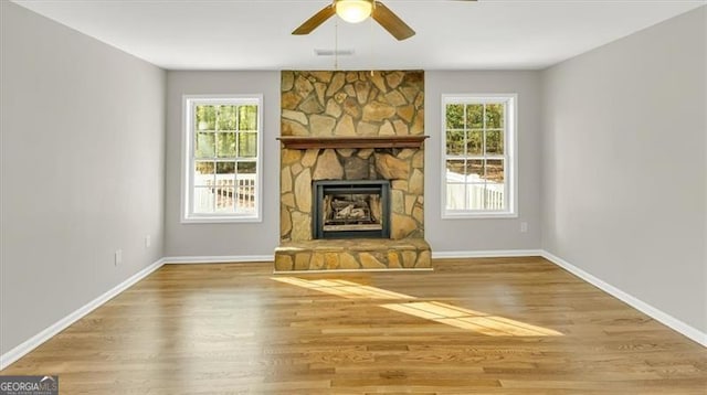 unfurnished living room with a stone fireplace, ceiling fan, plenty of natural light, and wood-type flooring