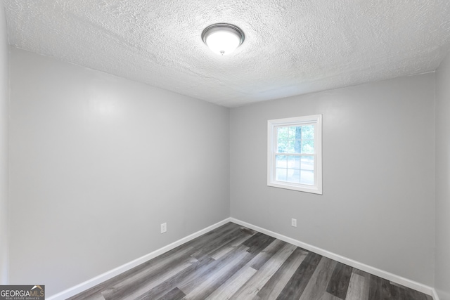 spare room featuring dark wood finished floors, a textured ceiling, and baseboards