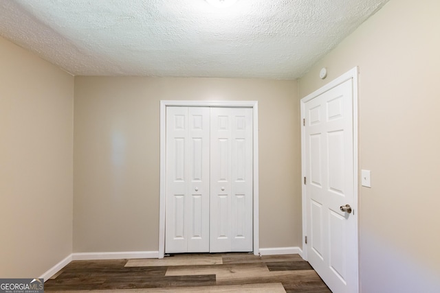 unfurnished bedroom featuring a textured ceiling, a closet, wood finished floors, and baseboards