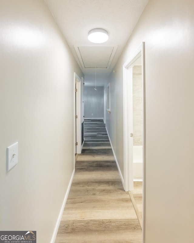 hallway featuring attic access, baseboards, and wood finished floors