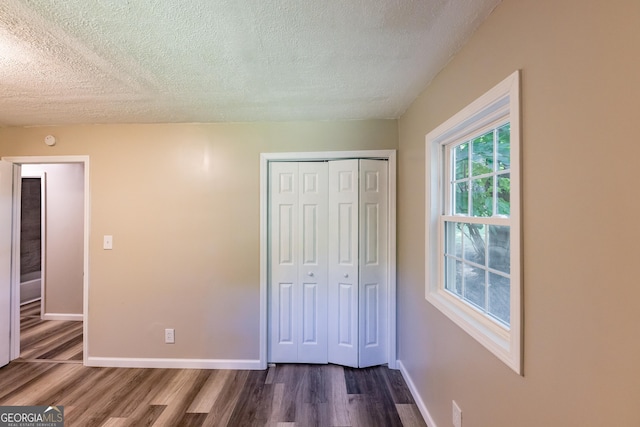 unfurnished bedroom with dark wood-style floors, a closet, a textured ceiling, and baseboards